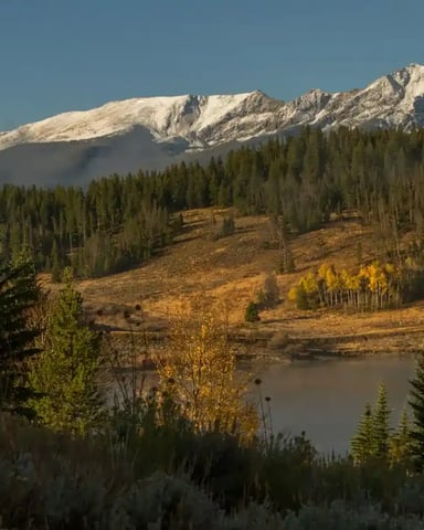 Snow-capped mountain range with autumn aspen trees and evergreen forest surrounding a calm lake
