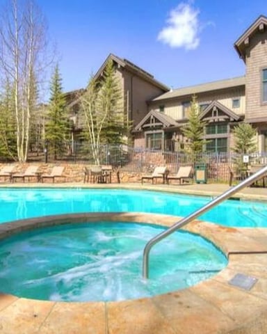 Resort pool and hot tub with lounge chairs, surrounded by pine trees and multi-story lodge buildings