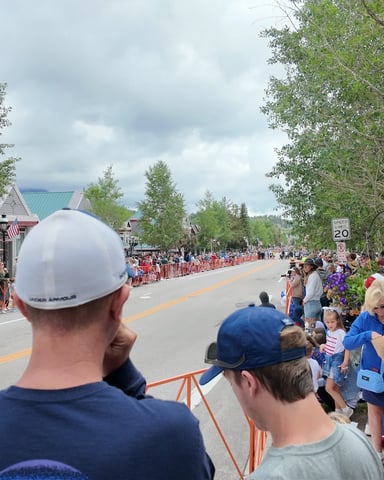 Crowd lining a main street in Breckenridge during a parade, with historic buildings and welcome sign visible