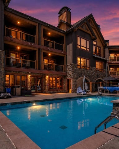 Luxury resort with illuminated pool at dusk, stone and timber buildings with lit windows, purple sunset sky