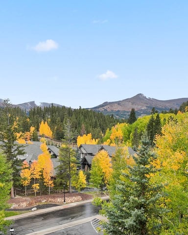 Mountain resort community in fall with golden aspens, evergreens, homes with gray roofs, and snow-capped peaks in distance