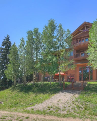 Modern wood-sided mountain home surrounded by aspen trees with mountain views and clear blue sky