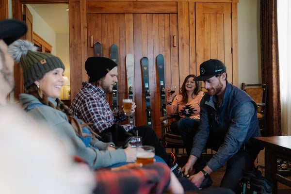 Group of people socializing indoors with skis displayed on wooden wall behind them