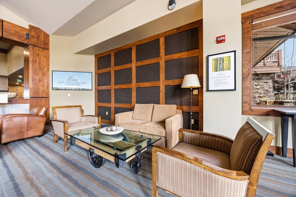 Upscale lodge living room with wood-framed furniture, glass coffee table, fireplace accent wall, and mountain views through windows