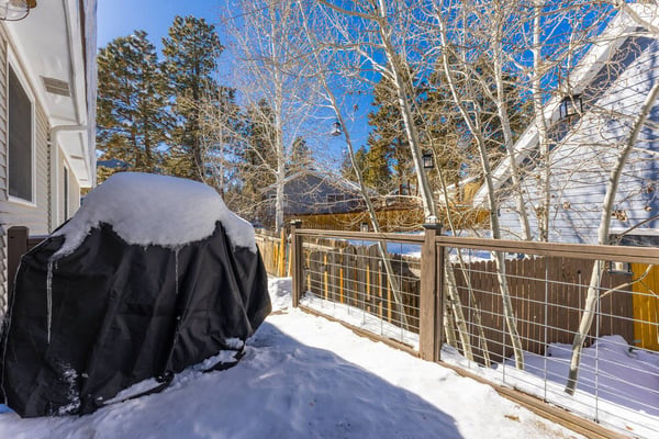 Snow-covered deck with black grill, wooden railing, bare aspen trees, and mountain view under clear blue sky