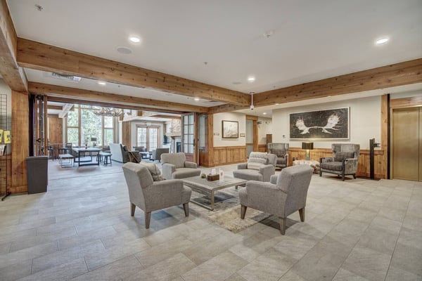 Spacious lodge lobby with exposed wood beams, tile flooring, upholstered seating, and large windows overlooking trees