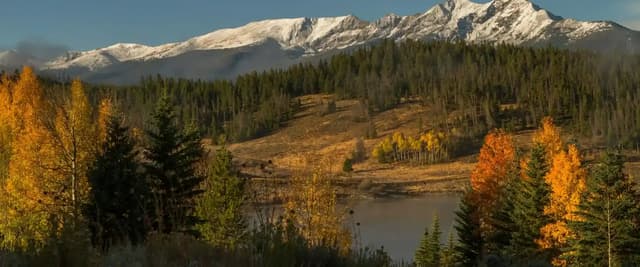 Snow-capped mountain range with autumn aspen trees and evergreen forest surrounding a calm lake