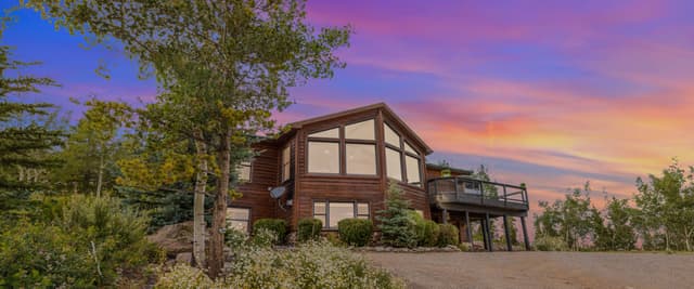 Modern wood cabin with large windows surrounded by trees and wildflowers at sunset