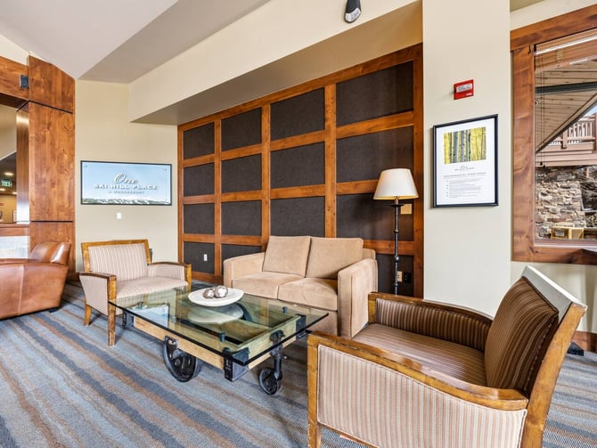 Upscale lodge lobby with wood-framed furniture, glass coffee table, stone fireplace, and mountain view through windows