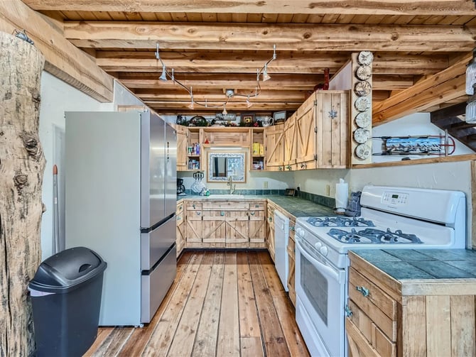 Rustic cabin kitchen with exposed wood beams, wooden cabinetry, stainless steel refrigerator, and white appliances